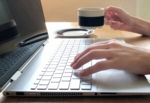 パソコン作業をしながらコーヒーを持つ女性の手