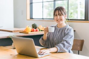 パソコンの前でコーヒーカップを持ってほほ笑む女性
