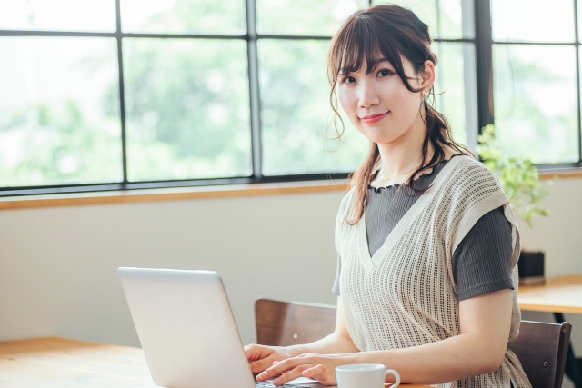 パソコンの前でこちらを向いてほほ笑む女性